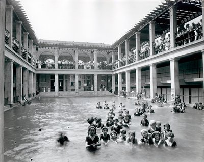 Horizontal, Black and White Photograph of a Swimming Pool with Two Story Balcony Supported by Columns. Onlookers Watch the Swimmers from the Second Level Balcony by William G. Swekosky